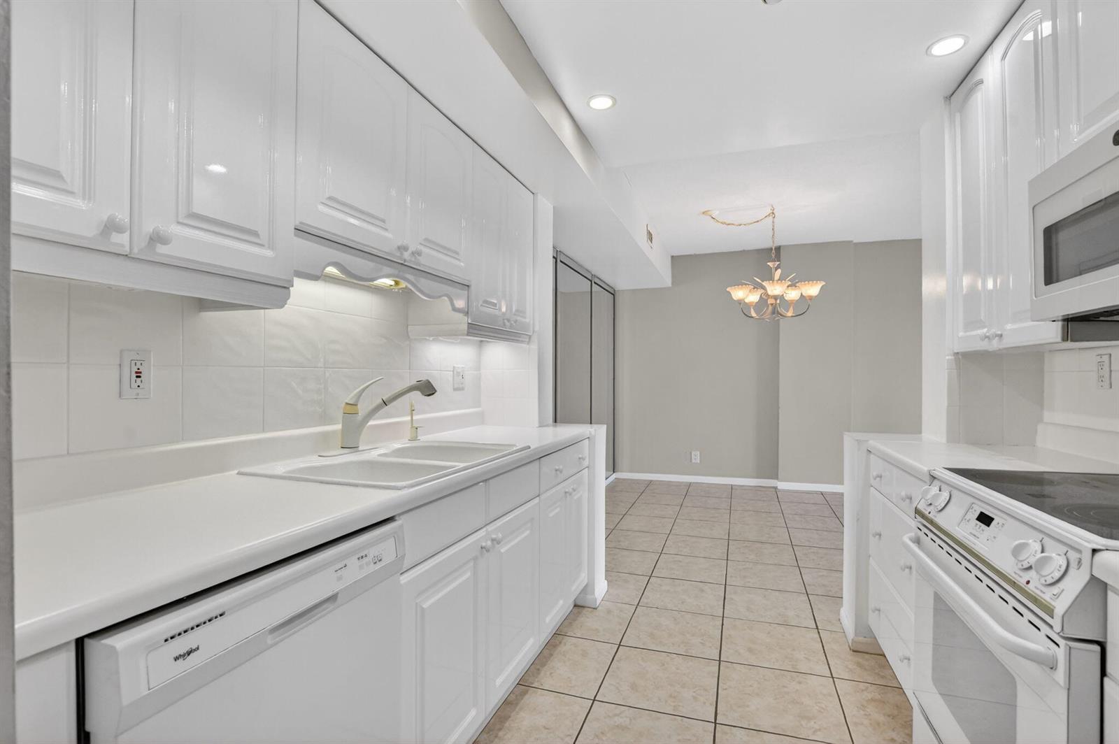 A galley-style kitchen features white cabinets, white appliances, and light-colored tile flooring — 250 NE 20th Street # 5220, Boca Raton FL 33431, BOCA RATON, FL
