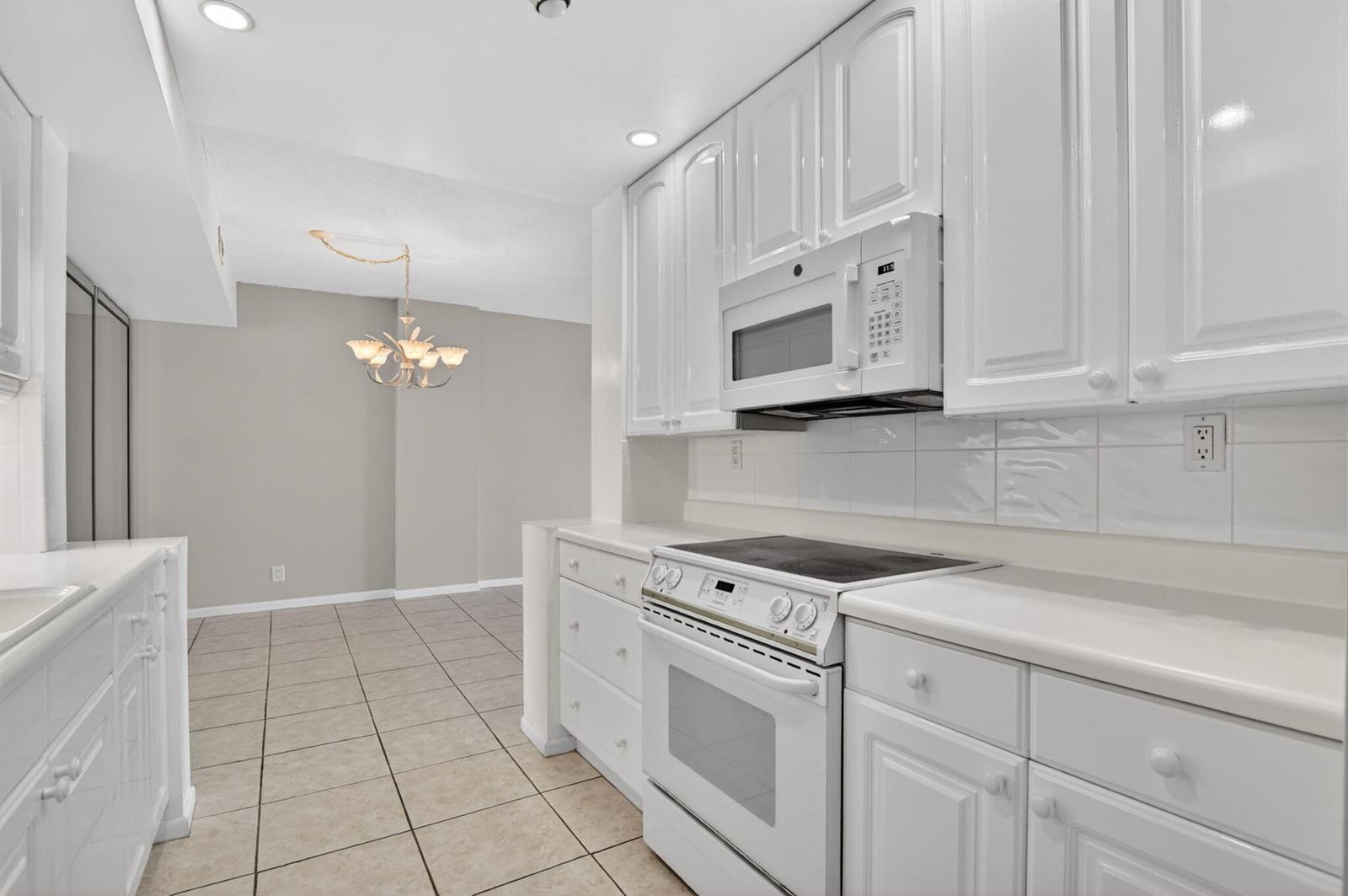A white kitchen with tile flooring, white cabinets, and a white stove and microwave — 250 NE 20th Street # 5220, Boca Raton FL 33431, BOCA RATON, FL
