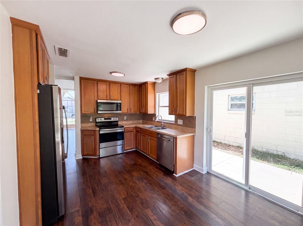 A kitchen with wood cabinets, stainless steel appliances, and dark wood flooring leads to a patio — 1030 MARTIN BOULEVARD UNIT 1, ORLANDO, FL