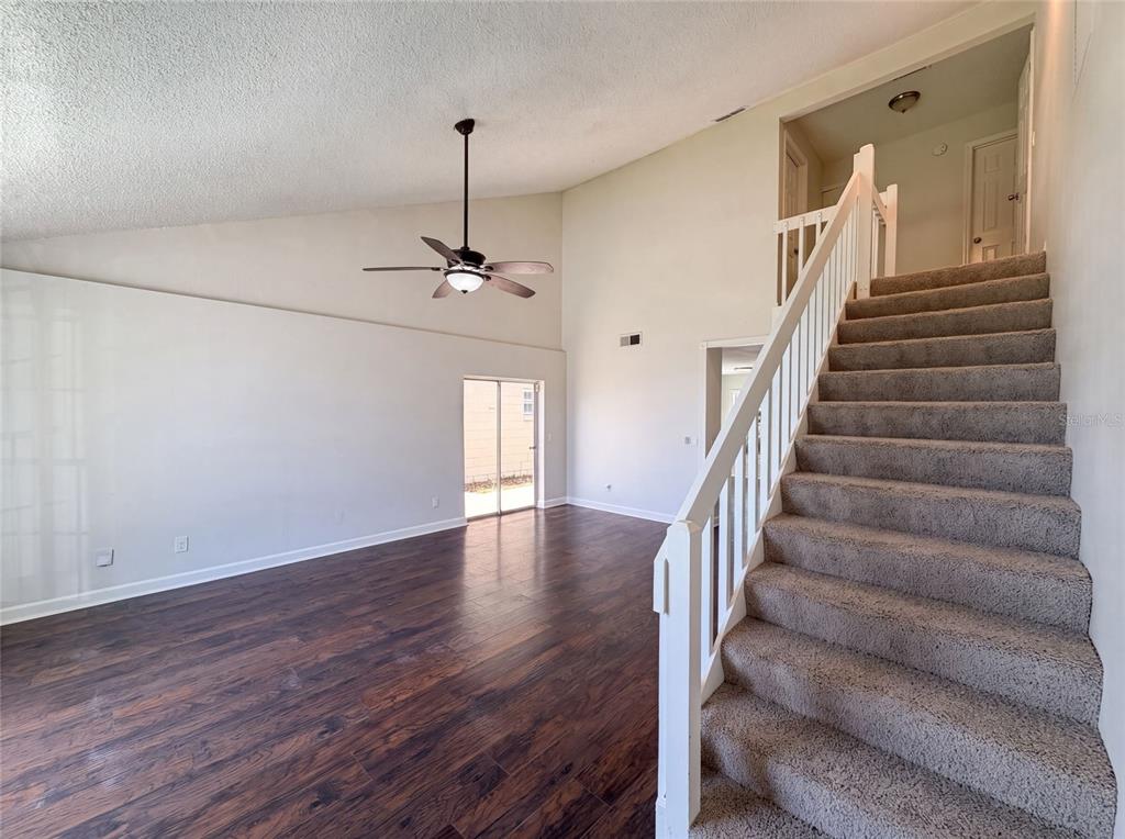 A living room with dark wood flooring, a vaulted ceiling, and carpeted stairs with white railings — 1030 MARTIN BOULEVARD UNIT 1, ORLANDO, FL