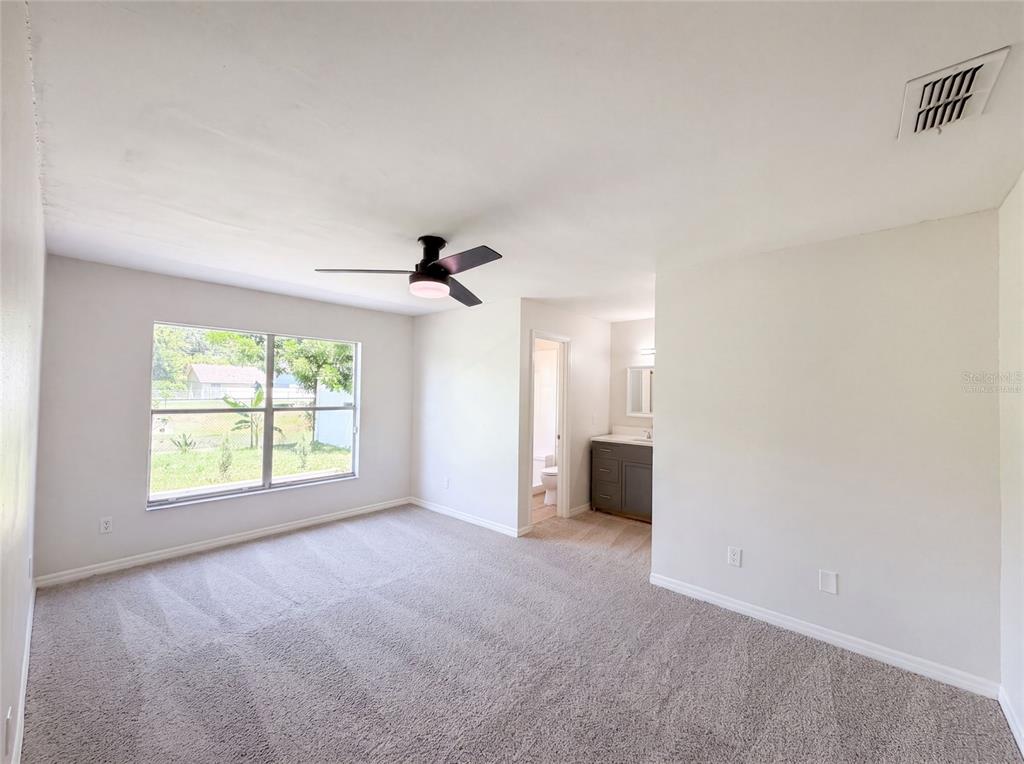 A bedroom with beige carpet, a ceiling fan, a window, and an attached bathroom — 1030 MARTIN BOULEVARD UNIT 1, ORLANDO, FL