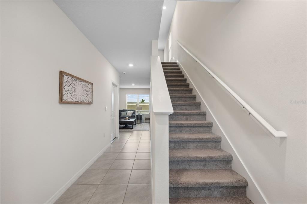 A hallway with tile flooring leads to a living area past a carpeted staircase — 30845 PENNY SURF LOOP, WESLEY CHAPEL, FL
