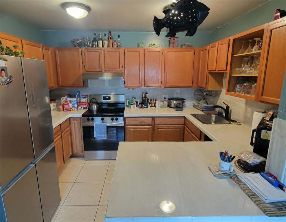 A kitchen features wood cabinets, stainless steel appliances, and a peninsula with a tiled countertop — 8446 WAVERLY ROAD N, ST PETERSBURG, FL