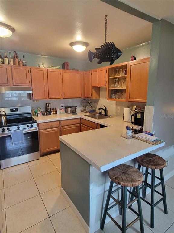 A kitchen features wood cabinets, white countertops, a stainless steel stove, and two bar stools — 8446 WAVERLY ROAD N, ST PETERSBURG, FL