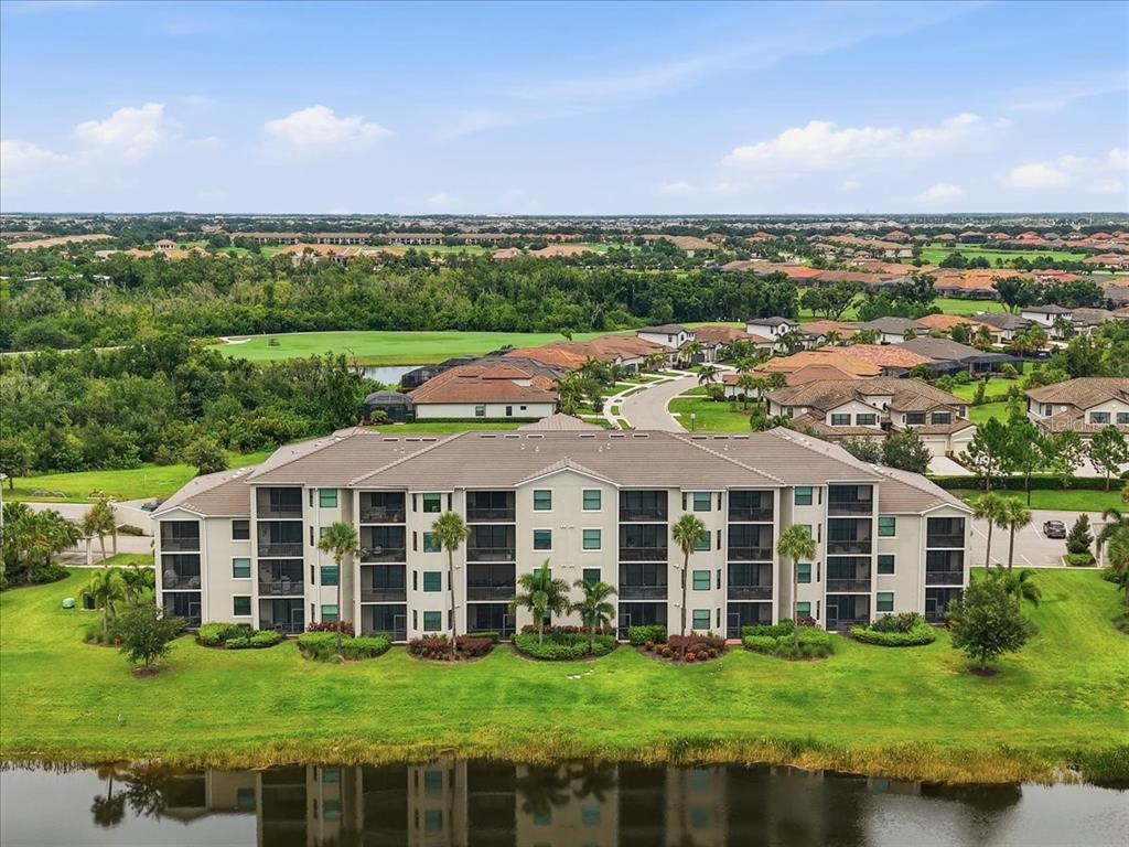 An aerial view of a multi-story apartment building situated next to a pond and golf course — 17520 GAWTHROP DRIVE UNIT 305, LAKEWOOD RANCH, FL