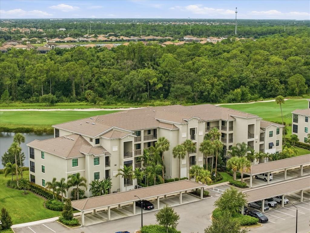An aerial view of a multi-story apartment building with covered parking and surrounding green space — 17520 GAWTHROP DRIVE UNIT 305, LAKEWOOD RANCH, FL