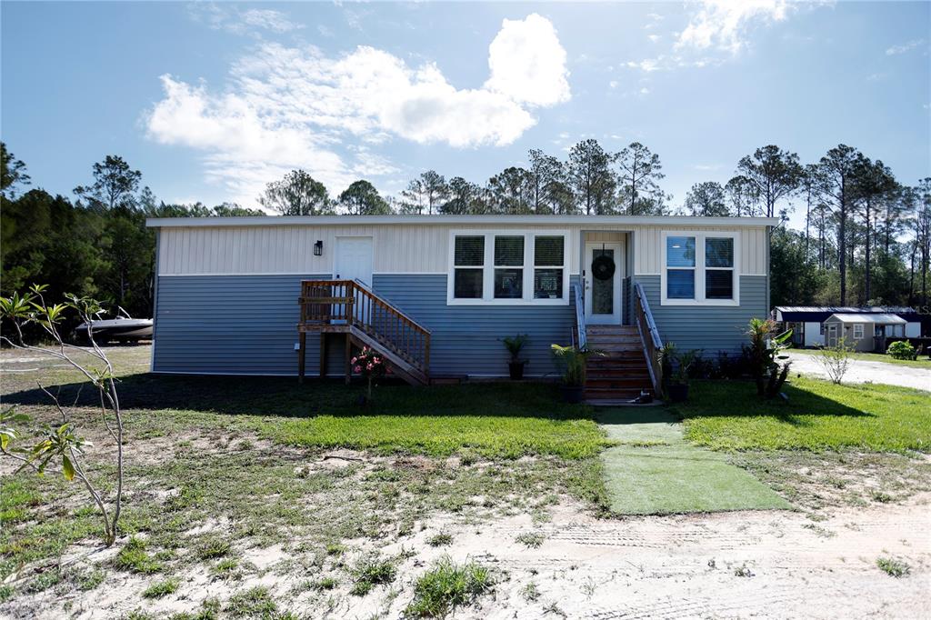 A two-tone manufactured home features a wooden staircase leading to a front entrance — 9060 KINDLEWOOD TRAIL, BROOKSVILLE, FL