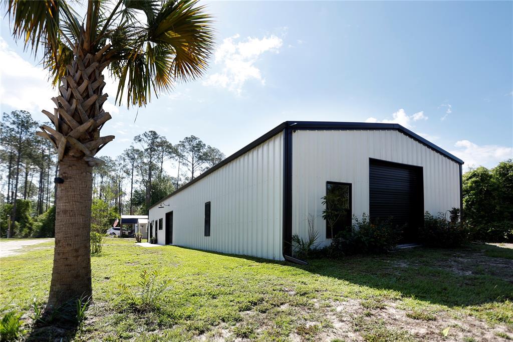 A white metal workshop building stands on a grassy lot next to a palm tree — 9060 KINDLEWOOD TRAIL, BROOKSVILLE, FL