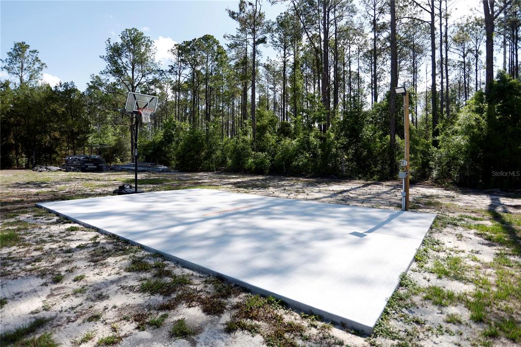 A concrete basketball court sits in a clearing surrounded by a dense forest — 9060 KINDLEWOOD TRAIL, BROOKSVILLE, FL