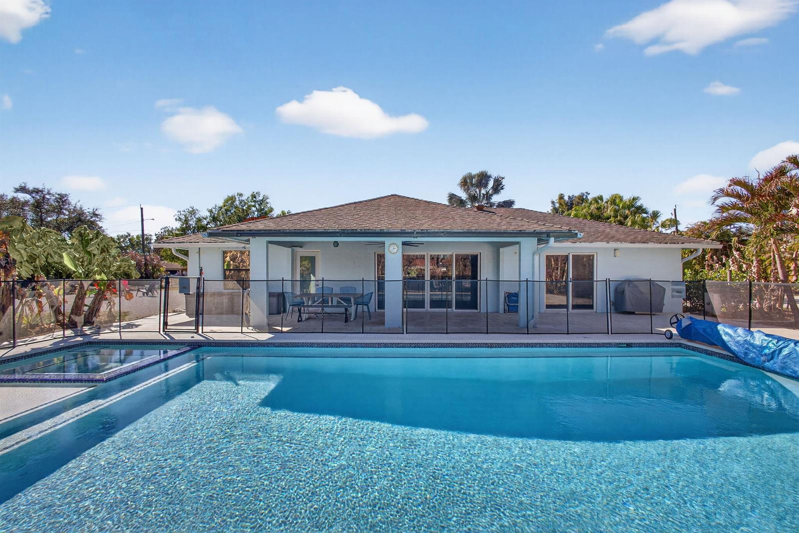 A backyard swimming pool with a safety fence sits in front of a single-story house — 16762 131st Way N, FL 33478, FL