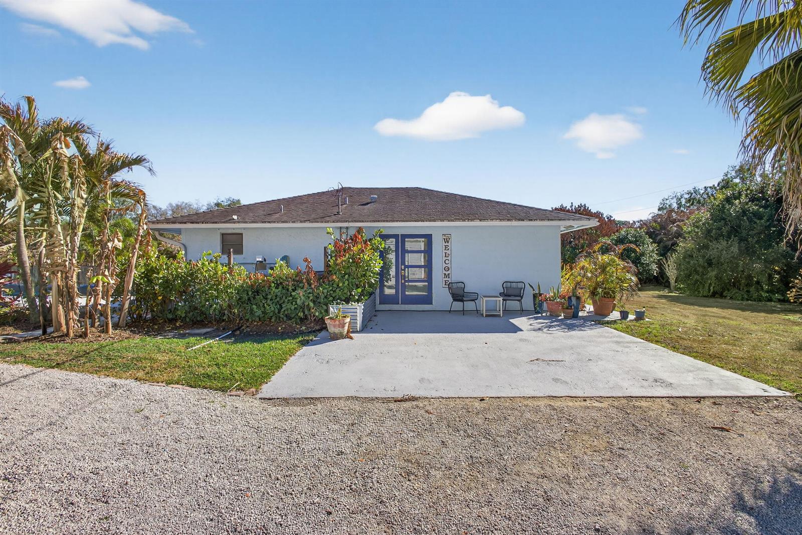 A single-story house with a blue door, a concrete patio, and surrounding tropical landscaping — 16762 131st Way N, FL 33478, FL