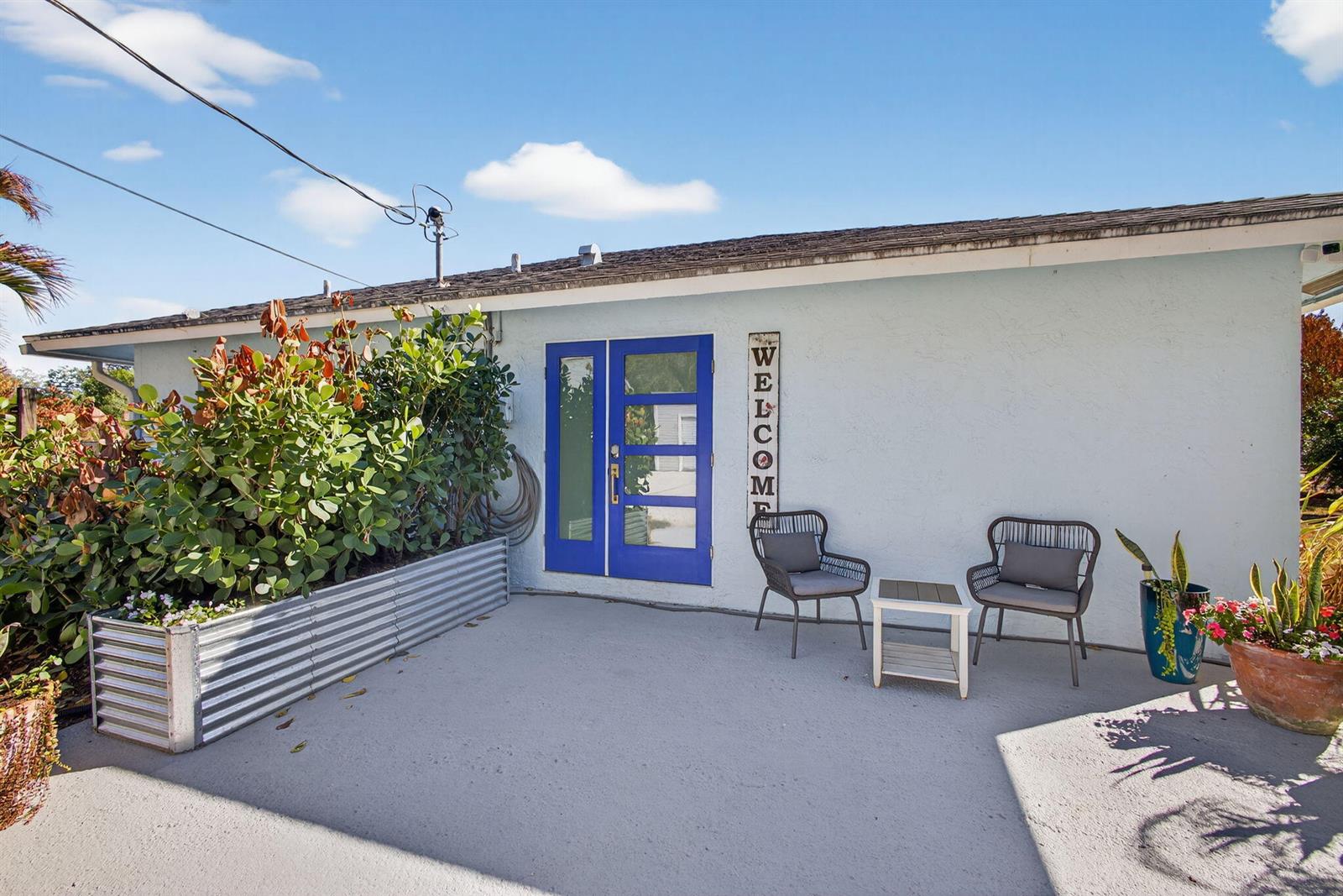 A light blue exterior wall features a blue double door, patio furniture, and metal planters — 16762 131st Way N, FL 33478, FL