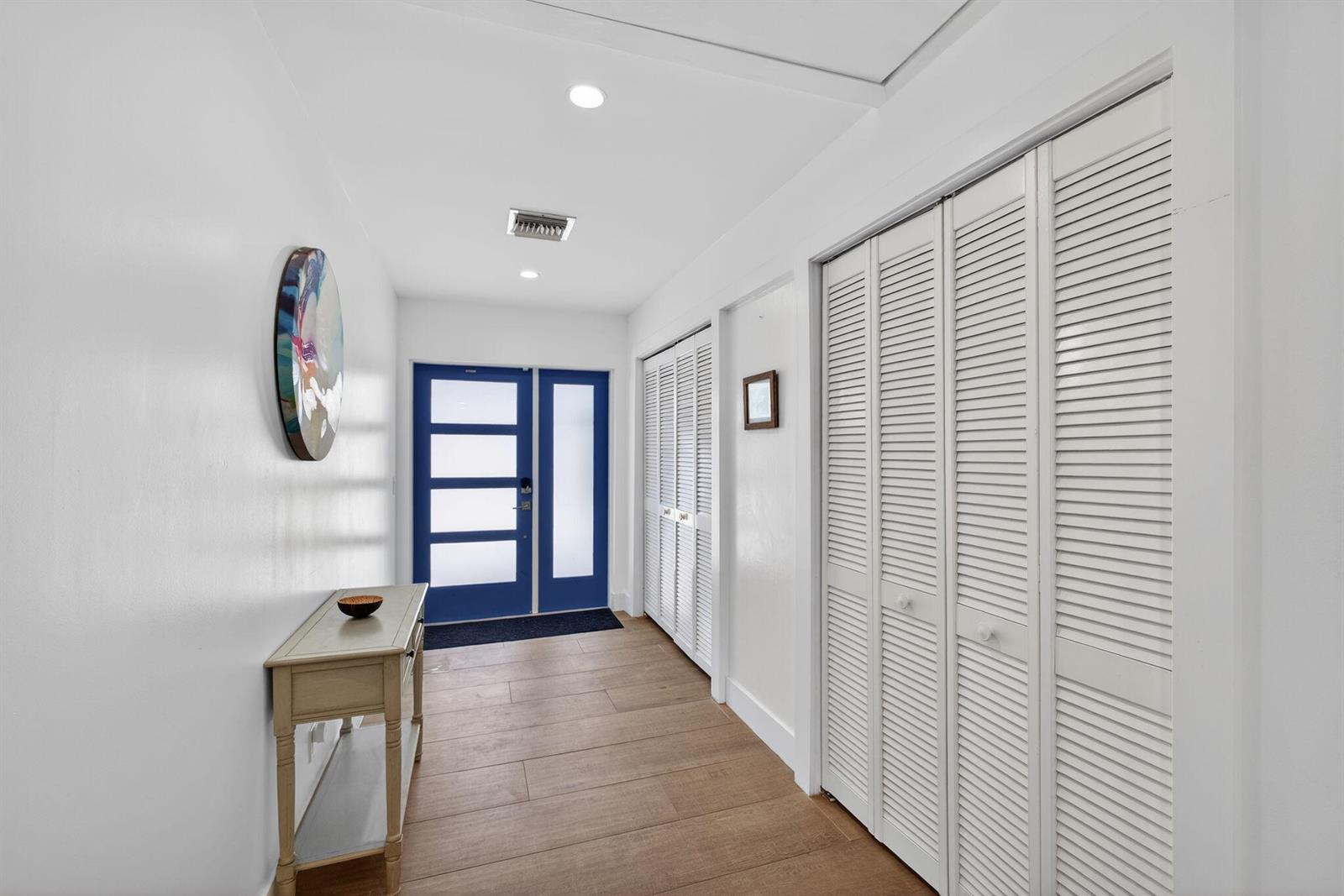 A bright entryway features wood-look tile flooring, white walls, louvered closet doors, and a blue door — 16762 131st Way N, FL 33478, FL