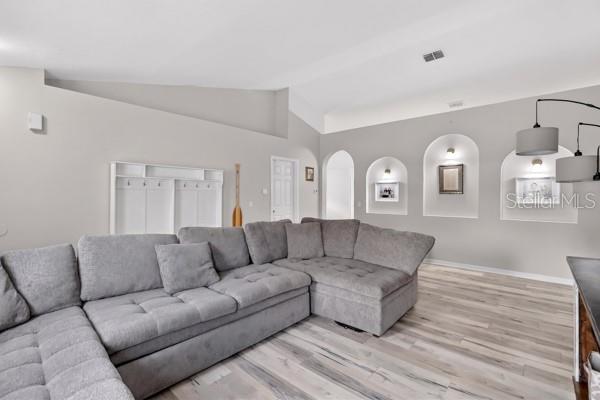 A living room features a large gray sectional sofa, light wood flooring, and arched wall niches — 3857 SLEEPY HILL OAKS LOOP, LAKELAND, FL
