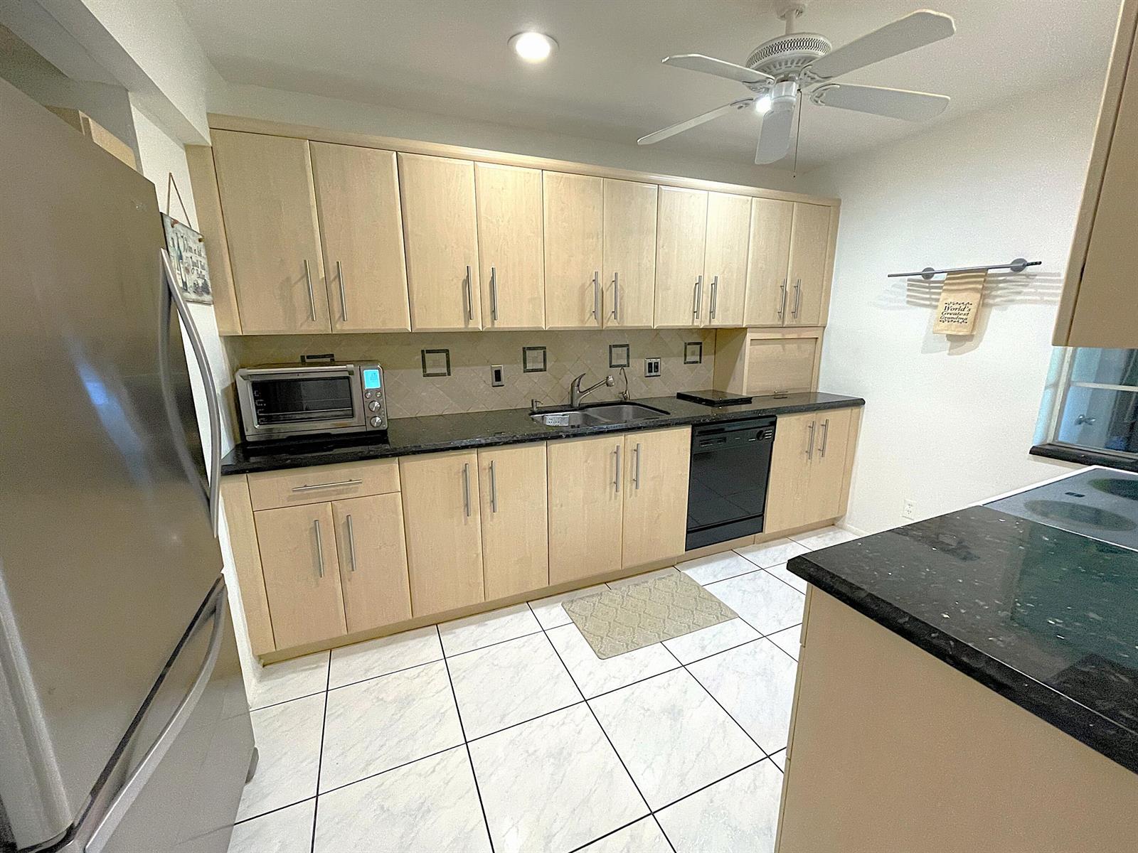 A kitchen features light wood cabinets, black countertops, stainless steel appliances, and white tiled floors — 2431 Del Aire Boulevard # d, Delray Beach FL 33445, DELRAY BEACH, FL