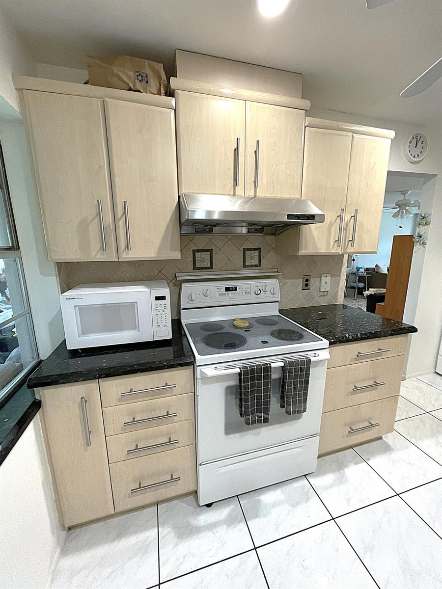 A kitchen features light wood cabinets, dark granite countertops, a white stove, and tiled floors — 2431 Del Aire Boulevard # d, Delray Beach FL 33445, DELRAY BEACH, FL