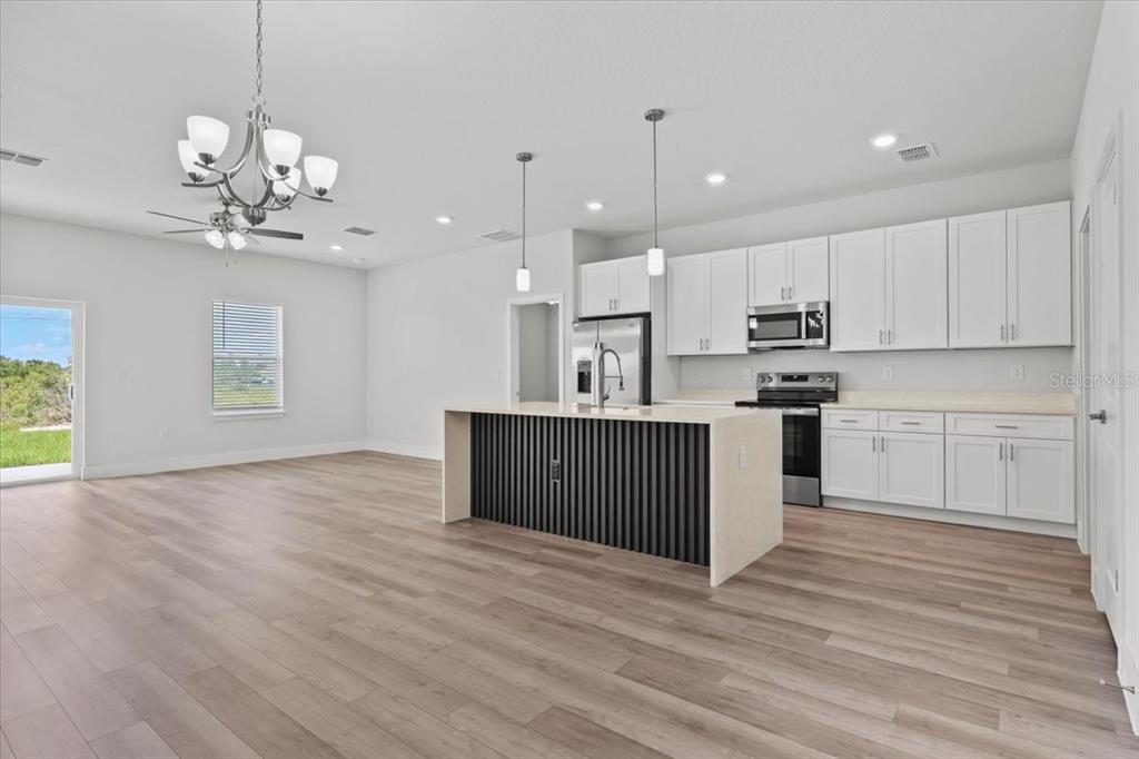 A modern kitchen features white cabinets, a black-slatted island, and light wood-look flooring — 2120 POINCIANA DRIVE, INDIAN LAKE ESTATES, FL