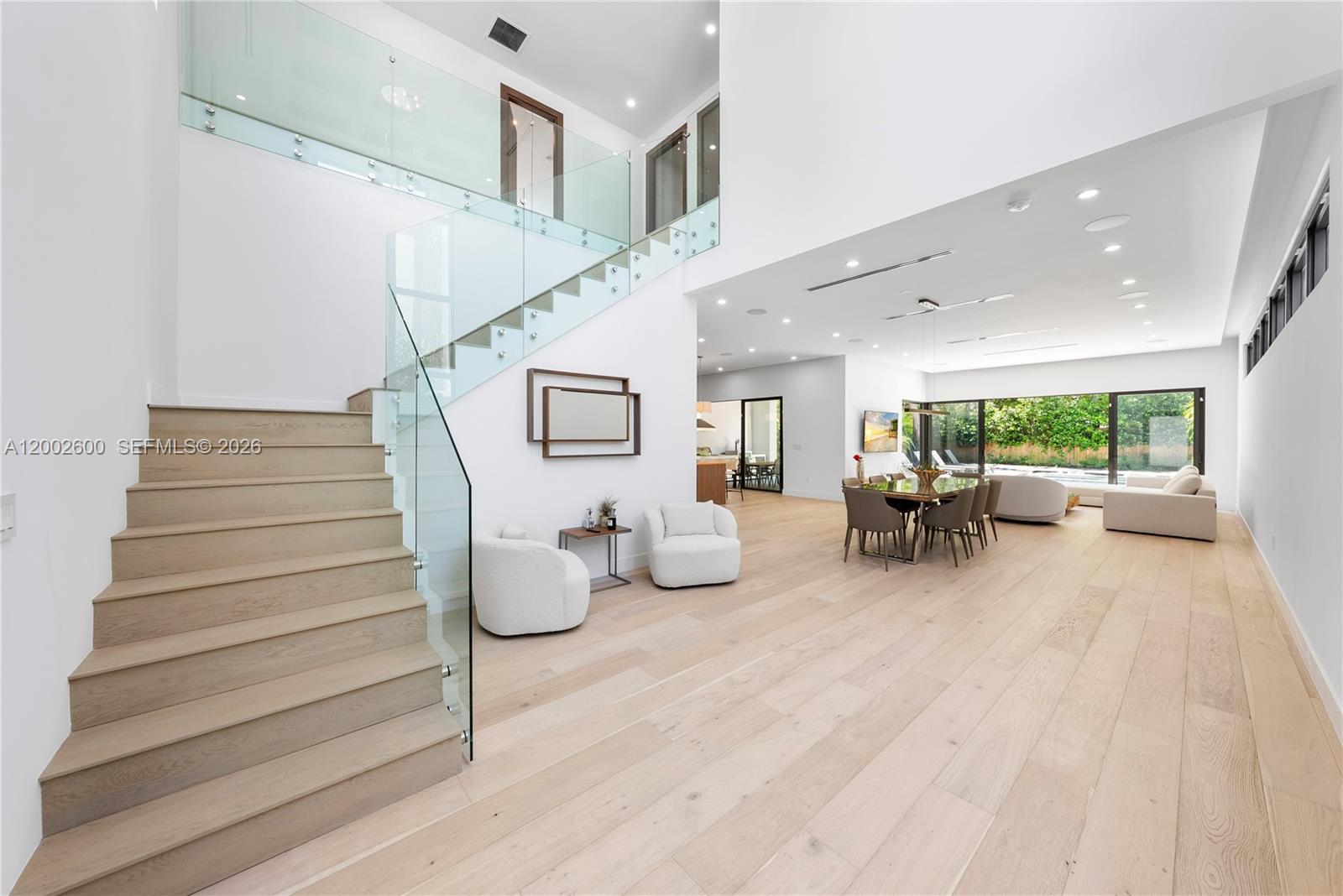 A modern, open-concept living and dining area features light wood floors and a glass staircase — 260 NW 47th St, Miami FL 33127, MIAMI, FL