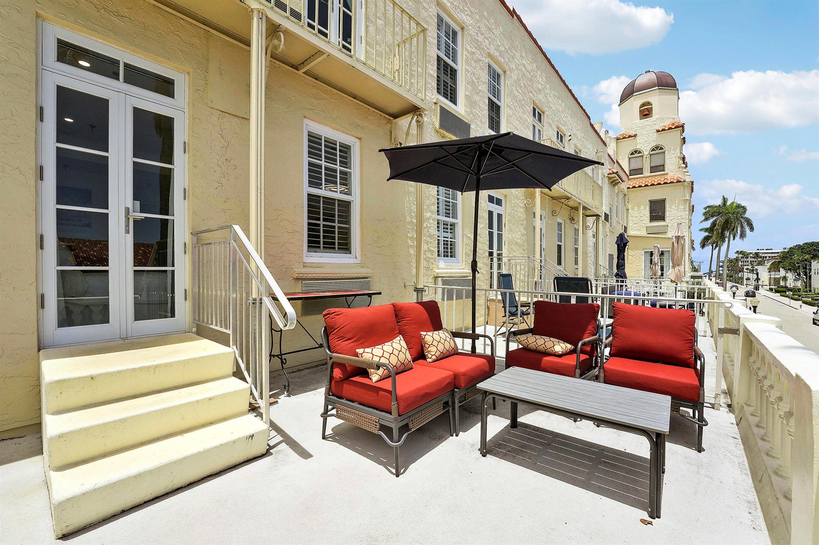 An outdoor patio features red cushioned furniture, a black umbrella, and stairs leading to doors — 235 Sunrise Avenue # 2011, Palm Beach FL 33480, PALM BEACH, FL