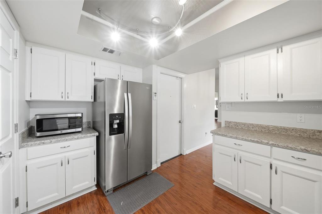 A kitchen with white cabinets, stainless steel appliances, granite-look countertops, and wood-style flooring — 1003 WHEELER PLACE, OVIEDO, FL