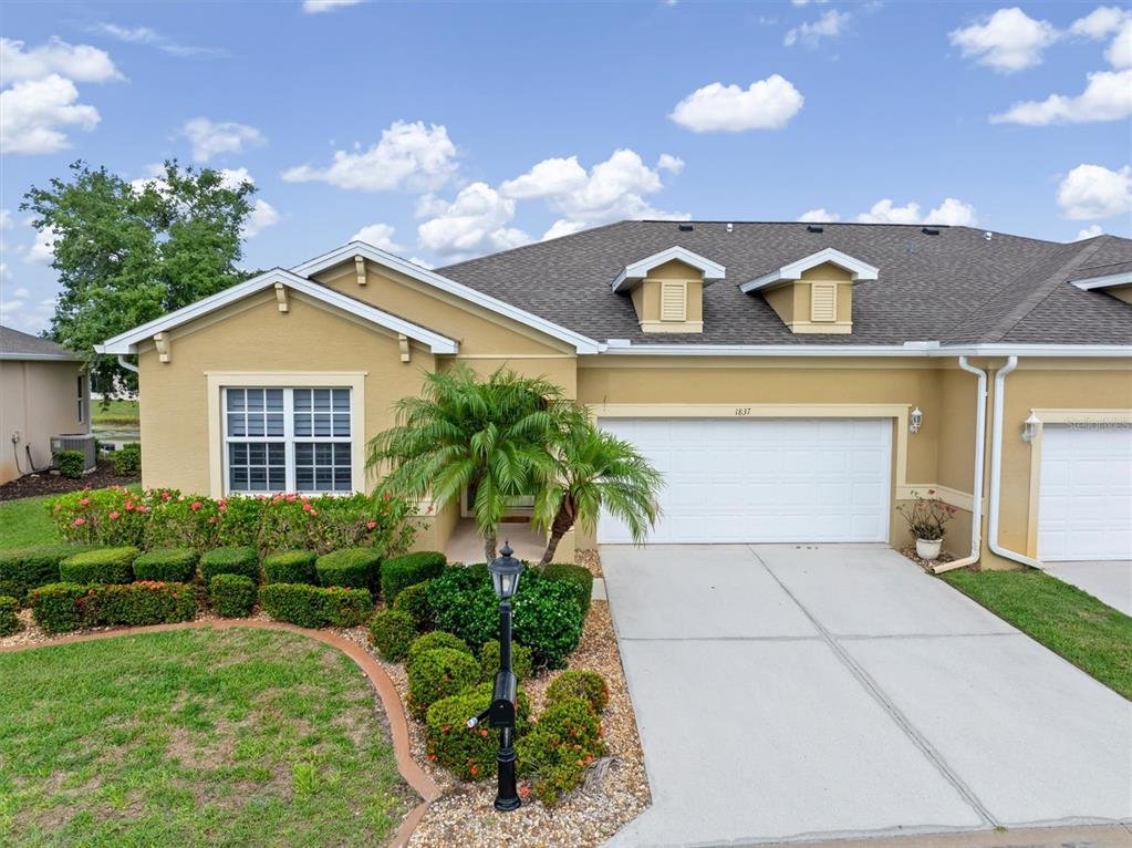 A tan single-story house features a two-car garage, a palm tree, and manicured landscaping — 1837 KNIGHTS BRIDGE TRAIL, PUNTA GORDA, FL
