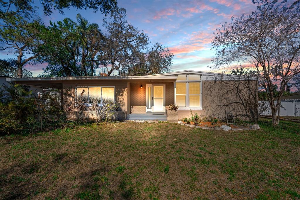 A single-story house with a flat roof, tan exterior, and a front porch at dusk — 206 LINDA AVENUE, TEMPLE TERRACE, FL