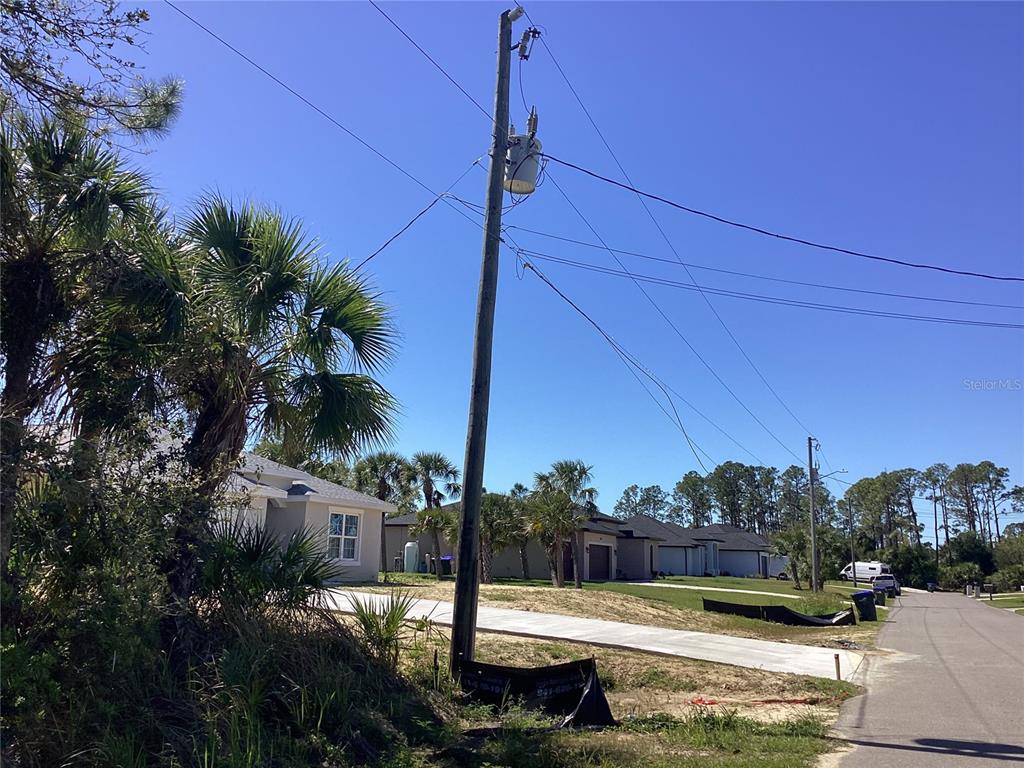 A utility pole stands in the foreground of a suburban street with new residential houses — BELLEVILLE TERRACE, NORTH PORT, FL