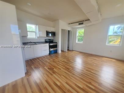 A kitchen with white cabinets and stainless steel appliances opens into a living area — 101 SE 2nd St # 2, Dania Beach FL 33004, DANIA BEACH, FL