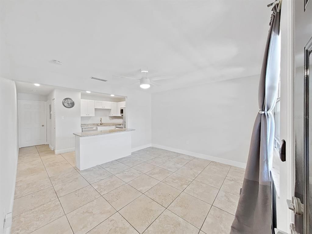 A bright, open-concept living area features light-colored tile flooring, a ceiling fan, and a kitchen — 2501 HARN BOULEVARD UNIT H39, CLEARWATER, FL