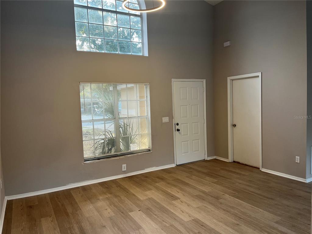 An empty room with light wood-look flooring, gray walls, a tall window, and two doors — 14904 WILD WOOD LILY COURT, ORLANDO, FL