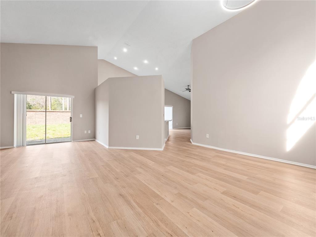 An empty living room features light wood-look flooring, vaulted ceilings, and a sliding glass door — 14904 WILD WOOD LILY COURT, ORLANDO, FL