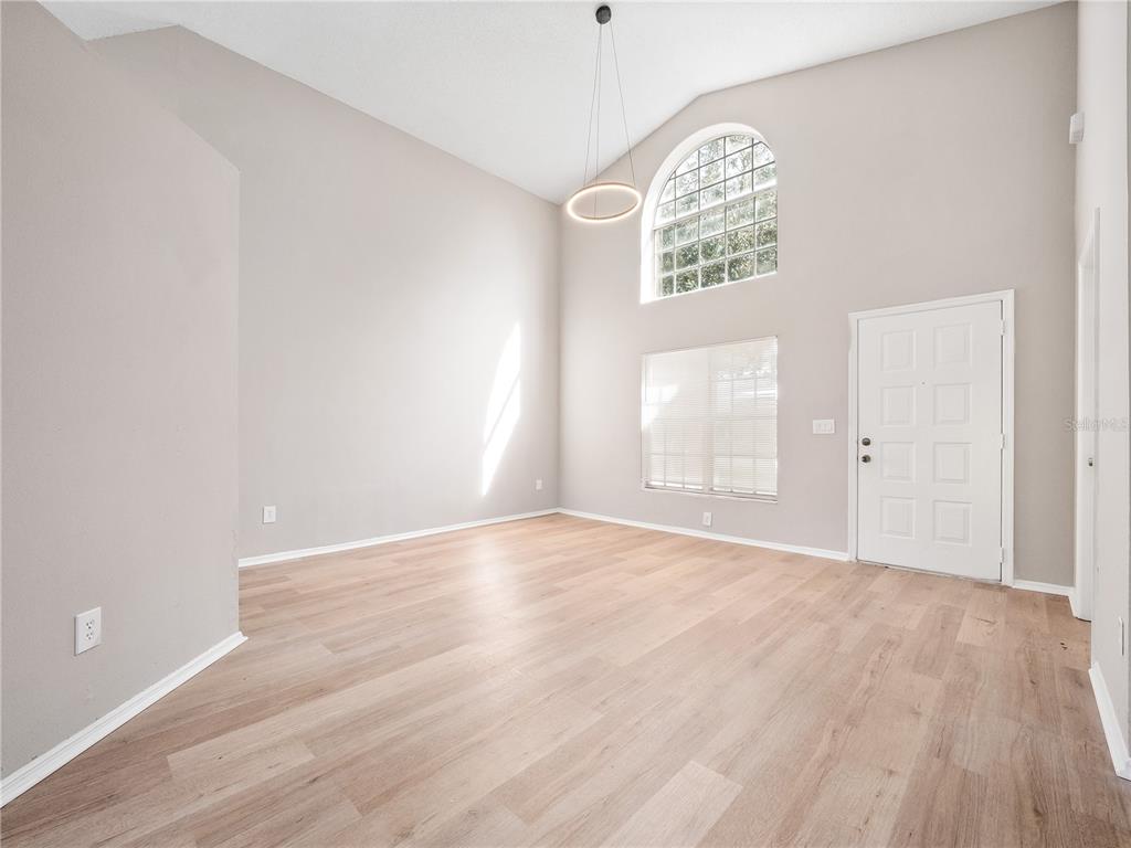 An empty living room with high ceilings, light wood-look flooring, and a large arched window — 14904 WILD WOOD LILY COURT, ORLANDO, FL