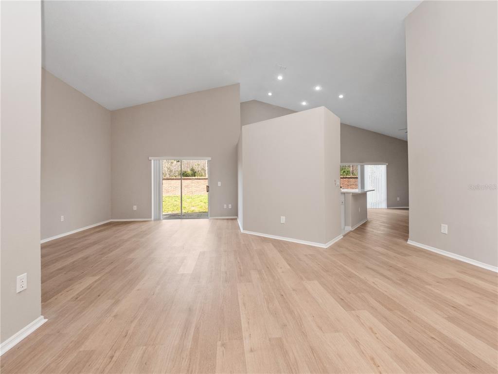 An open-concept living area features light wood-look flooring, vaulted ceilings, and a sliding glass door — 14904 WILD WOOD LILY COURT, ORLANDO, FL