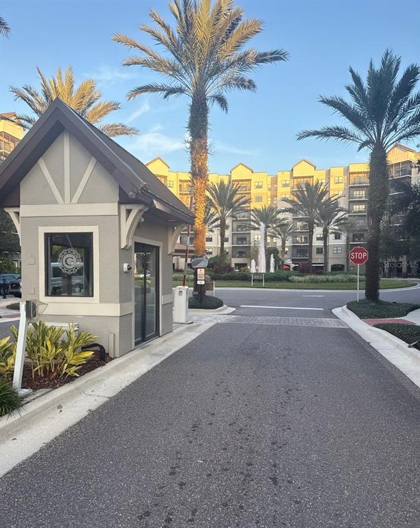 A gated entrance with a guardhouse, palm trees, and a multi-story apartment building in background — 14501 GROVE RESORT AVENUE UNIT 2528, WINTER GARDEN, FL