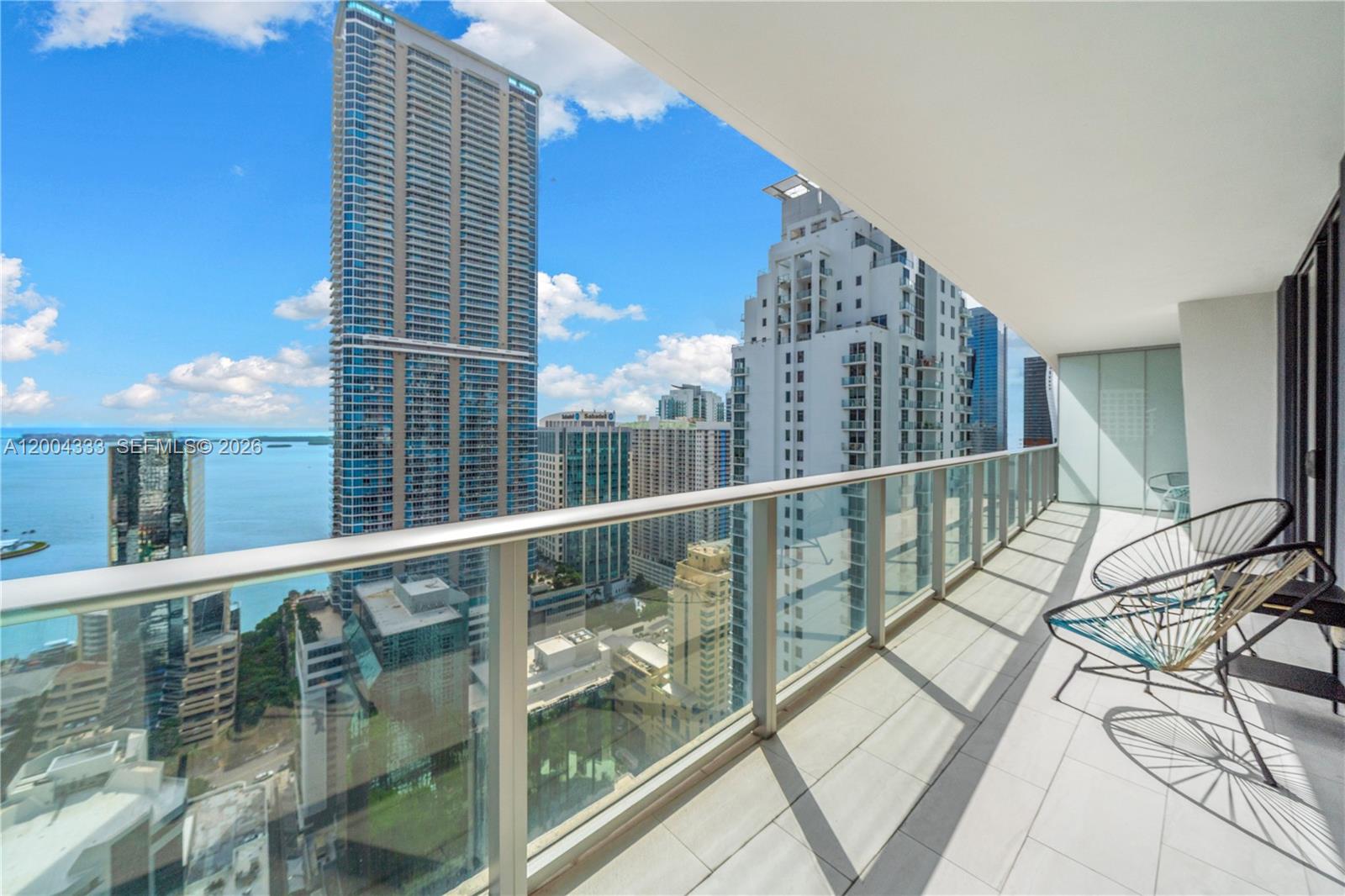 A high-rise balcony features a glass railing, tiled flooring, and two chairs overlooking the city — 1010 Brickell Ave # 3904, Miami FL 33131, MIAMI, FL