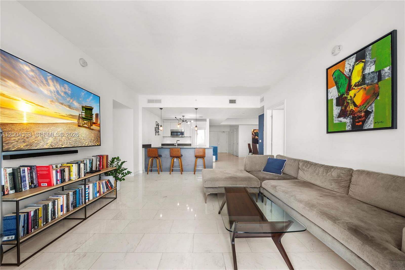 A living room features a large television, a bookshelf, a sectional sofa, and an open kitchen — 1010 Brickell Ave # 3904, Miami FL 33131, MIAMI, FL