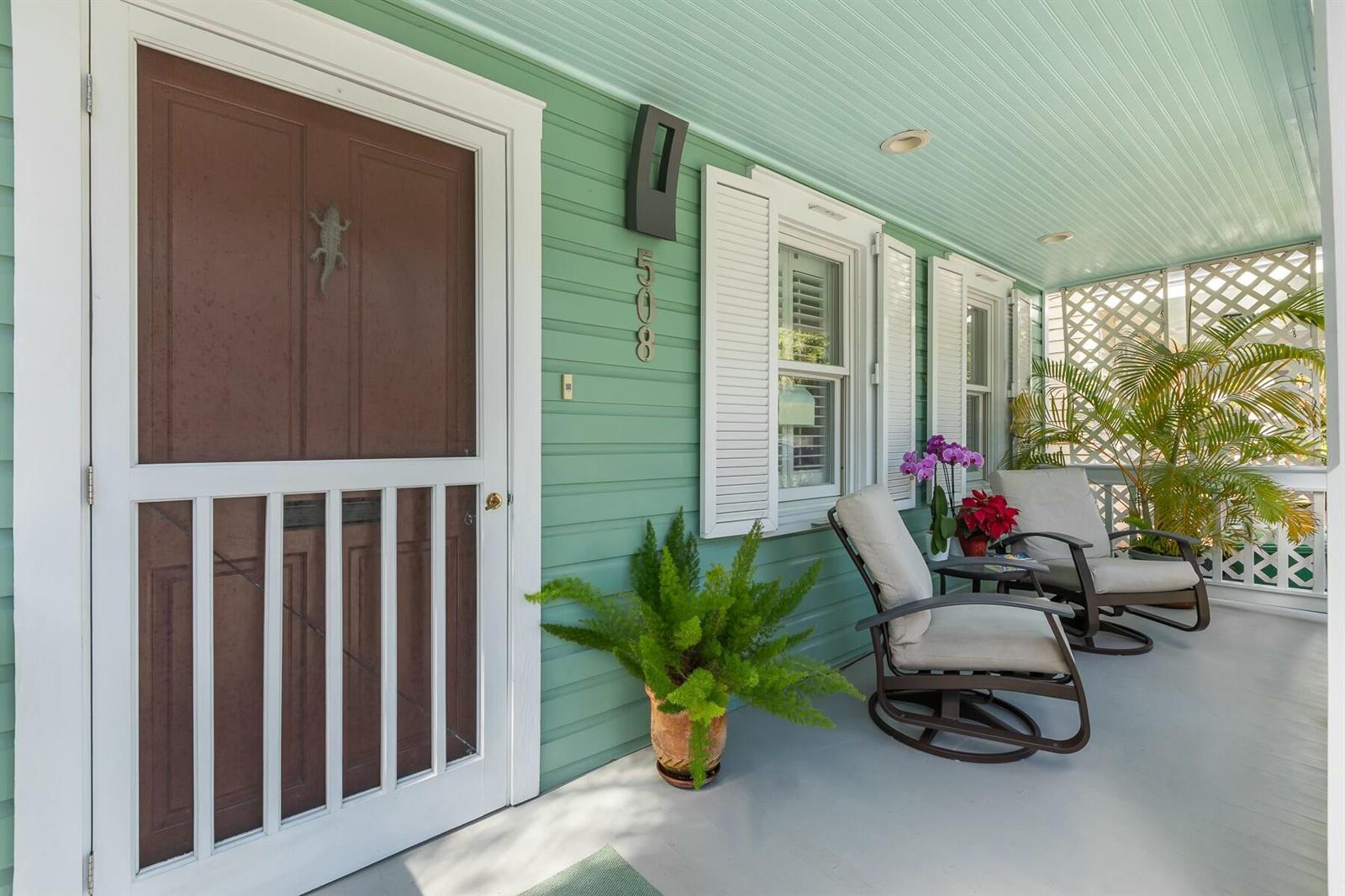 A covered front porch with light green siding, a screen door, and two outdoor chairs — 508 Grinnell Street, Key West FL 33040, KEY WEST, FL