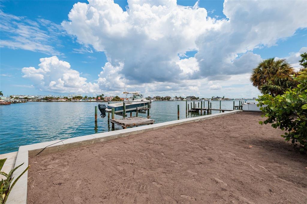 A sandy waterfront lot features a boat lift with a boat and a wooden dock — 216 PUNTA VISTA DRIVE, ST PETE BEACH, FL