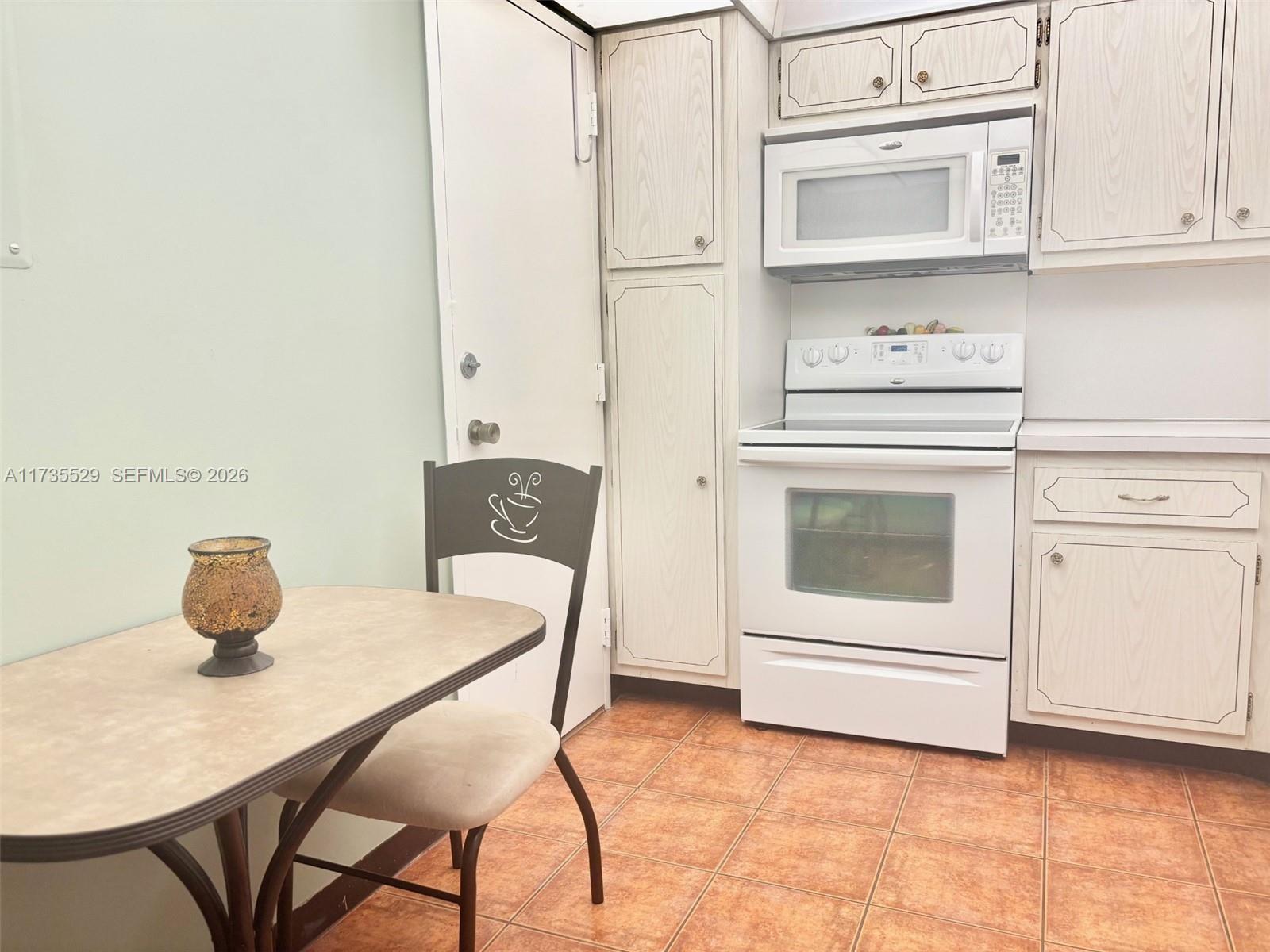 A kitchen features white cabinets, a white stove, a microwave, and a small dining table — 1965 S Ocean Dr # 11N, Hallandale Beach FL 33009, HALLANDALE BEACH, FL