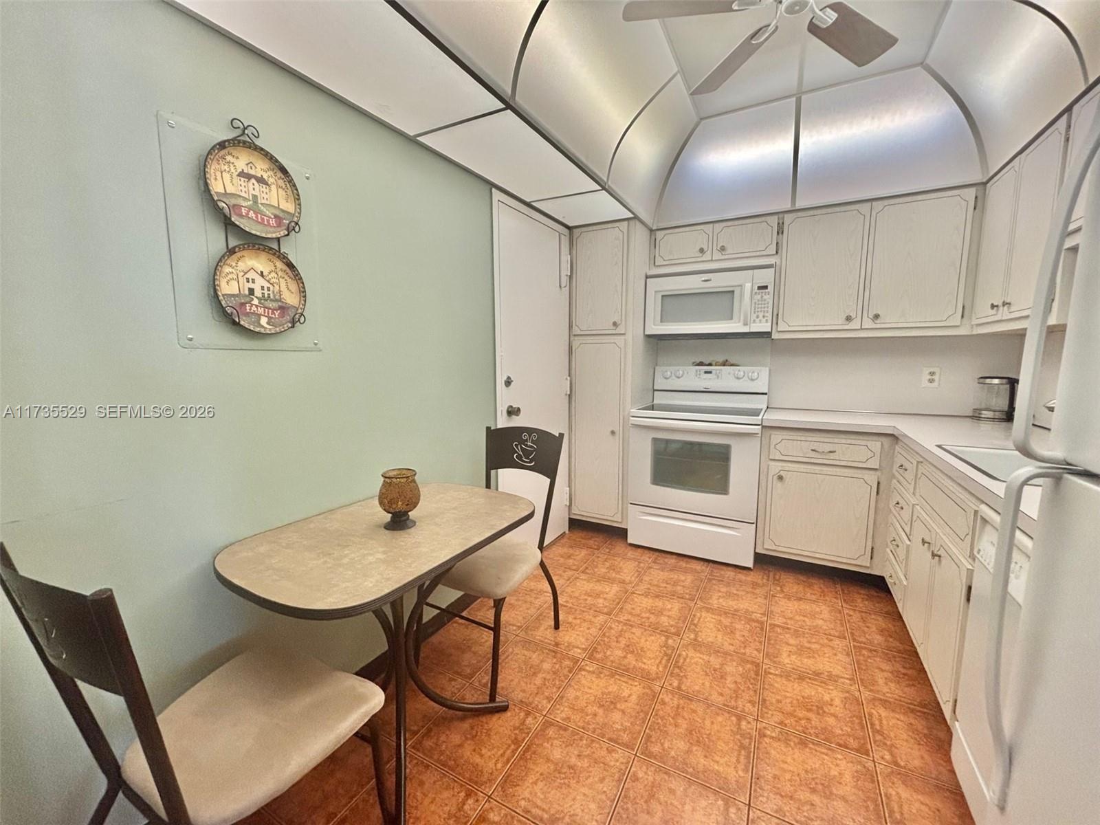 A kitchen features light-colored cabinets, white appliances, a small dining table, and terracotta-colored floor tiles — 1965 S Ocean Dr # 11N, Hallandale Beach FL 33009, HALLANDALE BEACH, FL