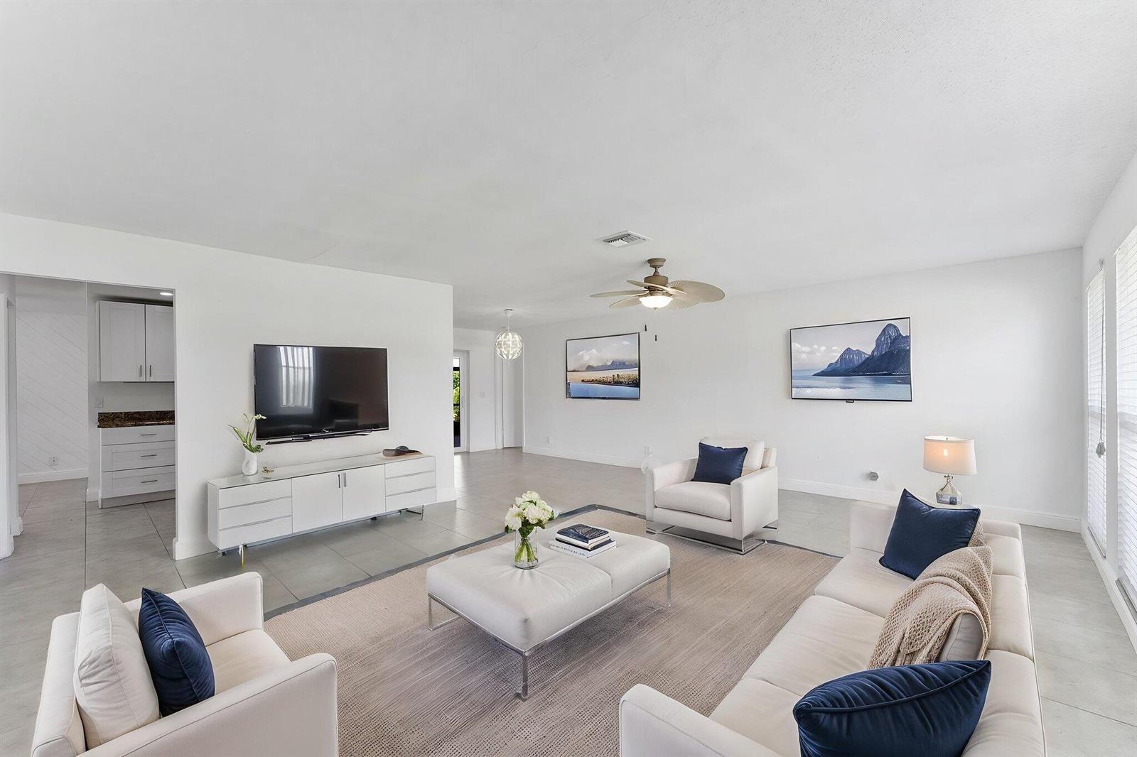 A bright living room features white furniture, a large area rug, and two wall-mounted televisions — 6396 Whispering Wind Way, Delray Beach FL 33484, DELRAY BEACH, FL