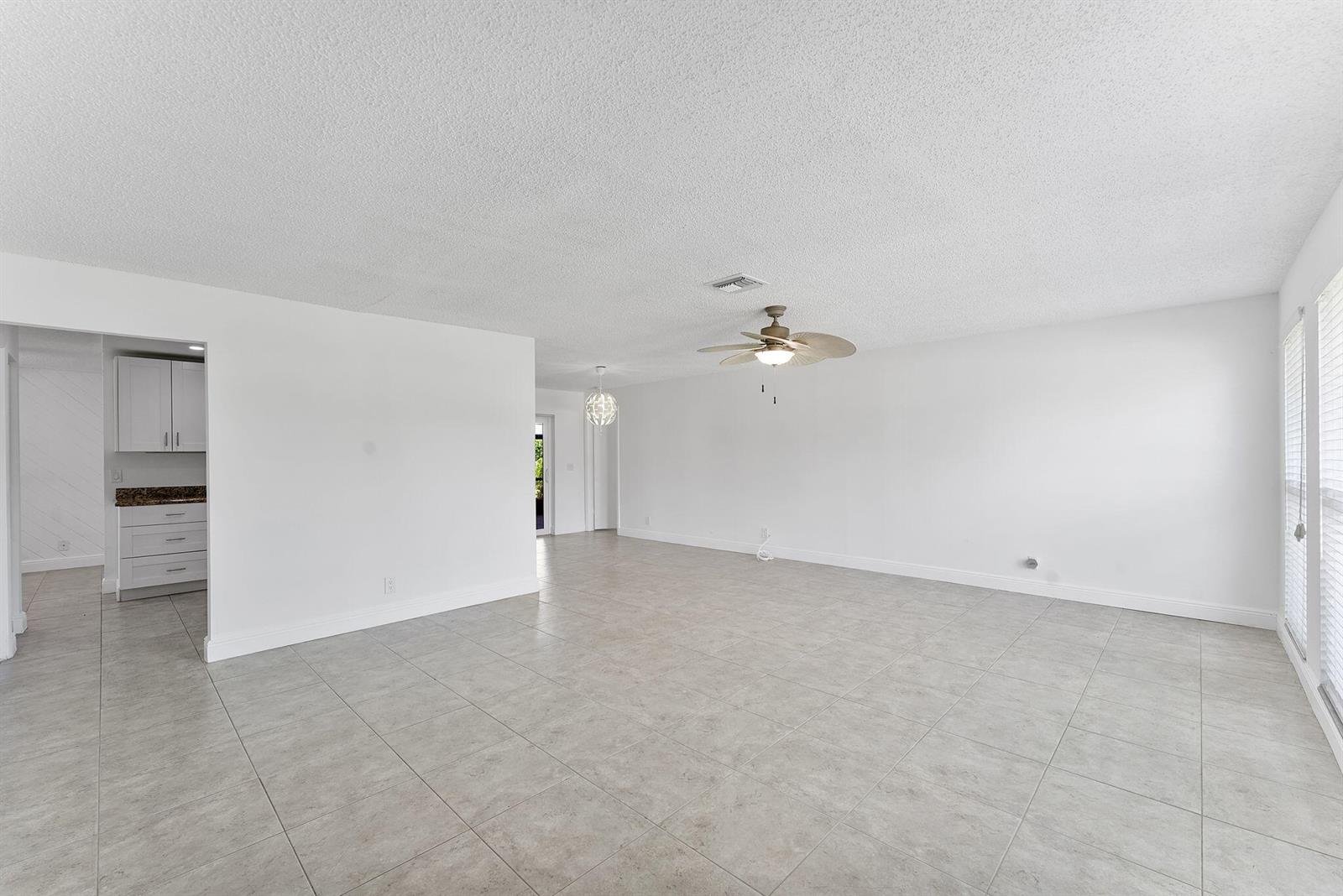 An open-concept living area features white walls, light-colored tile flooring, and a ceiling fan — 6396 Whispering Wind Way, Delray Beach FL 33484, DELRAY BEACH, FL
