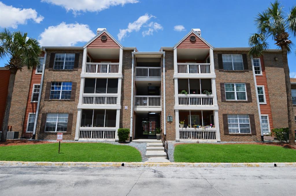 A three-story brick apartment building with screened balconies and a central stairwell entrance — 10200 GANDY BOULEVARD N UNIT 1313, ST PETERSBURG, FL