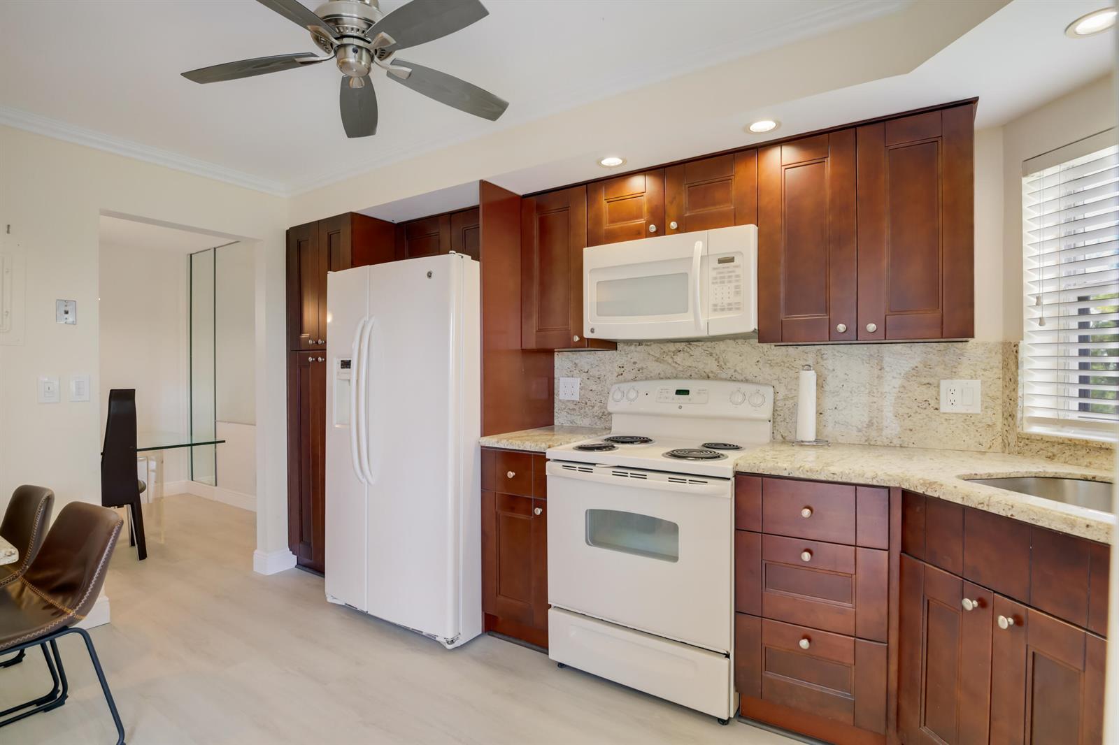 A kitchen with dark wood cabinets, white appliances, granite countertops, and a ceiling fan — 3593 Birdie Drive # 507, Lake Worth FL 33467, LAKE WORTH, FL