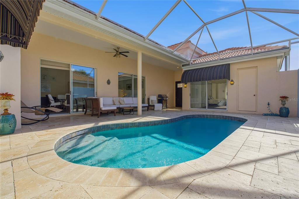 A screened-in patio features a swimming pool, travertine pavers, and sliding glass doors — 8717 54TH AVENUE E UNIT NA, BRADENTON, FL