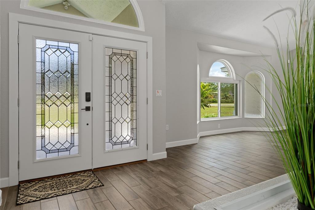 An entryway with a double glass-paneled front door, light gray walls, and wood-look tile flooring — 4200 W PINE RIDGE BOULEVARD, BEVERLY HILLS, FL