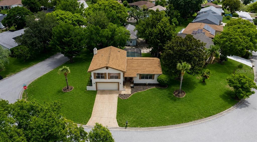 An aerial view shows a single-story house with a tan roof and driveway on a corner lot — 8609 VILLAGE MILL ROW, HUDSON, FL