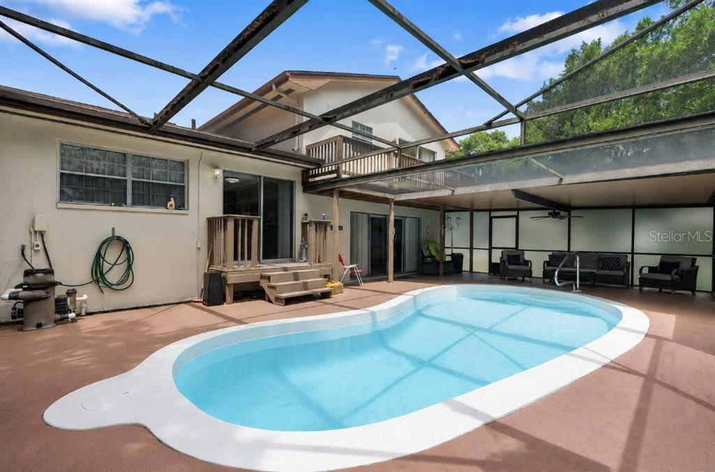 A backyard swimming pool is enclosed by a screened-in patio attached to a two-story house — 8609 VILLAGE MILL ROW, HUDSON, FL