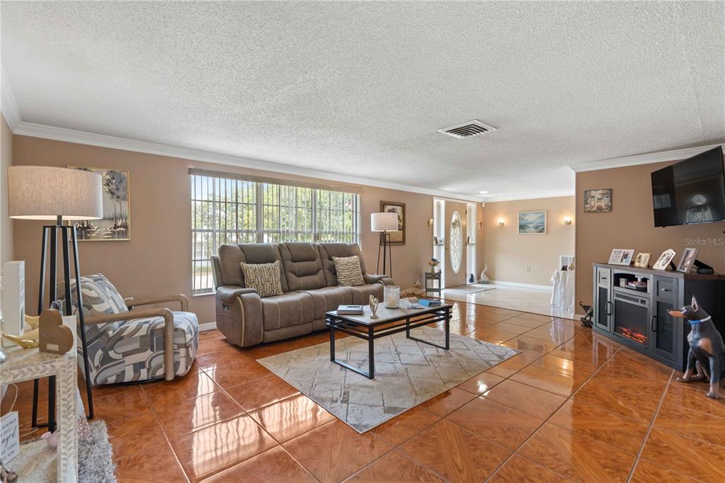 A living room features glossy tile floors, a gray sofa, and a television on a stand — 8609 VILLAGE MILL ROW, HUDSON, FL