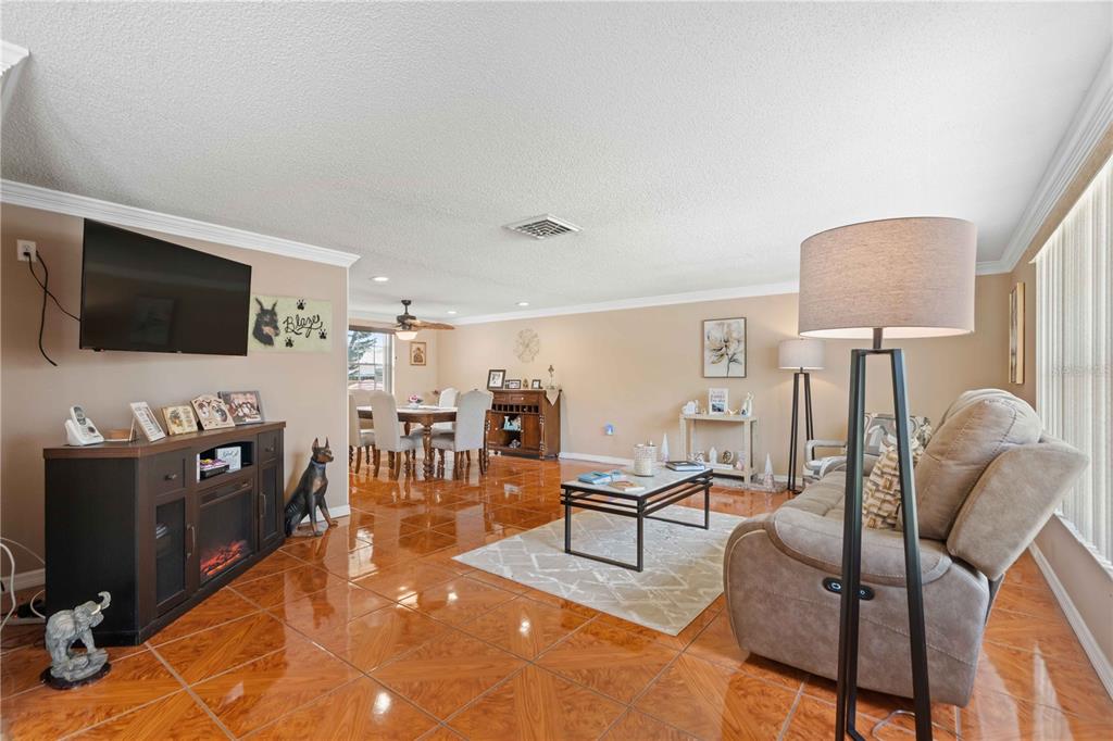 A living room with glossy tile floors, a television console, and a beige reclining sofa — 8609 VILLAGE MILL ROW, HUDSON, FL